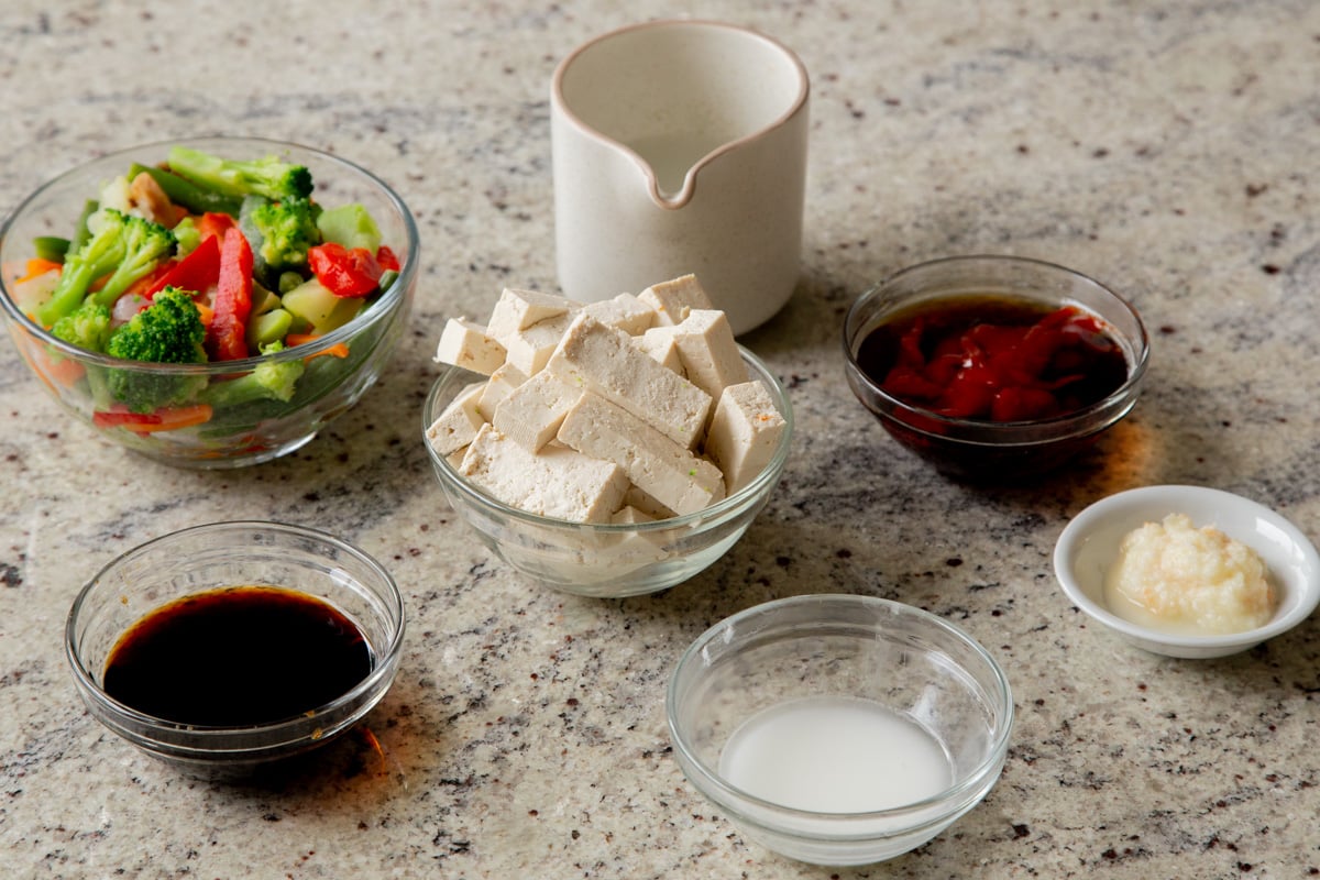tofu and other stir fry ingredients in bowls on a kitchen counter