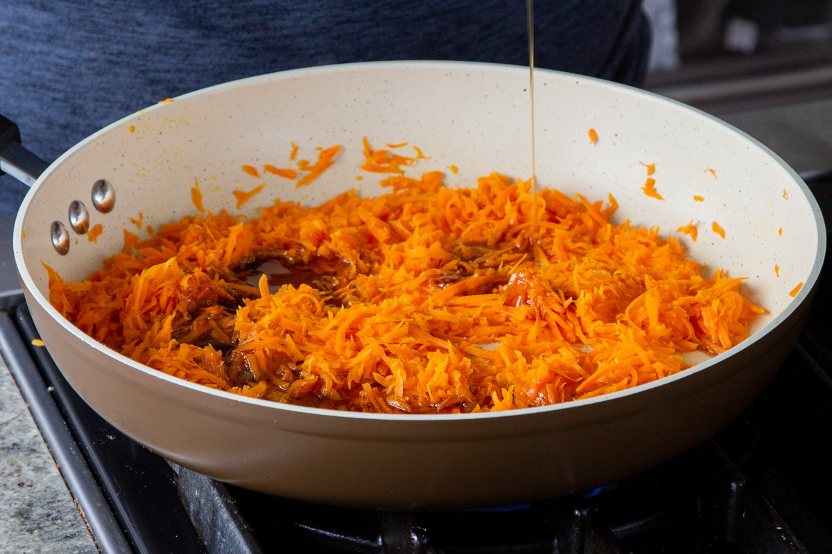 adding maple syrup to the pan of shredded carrots