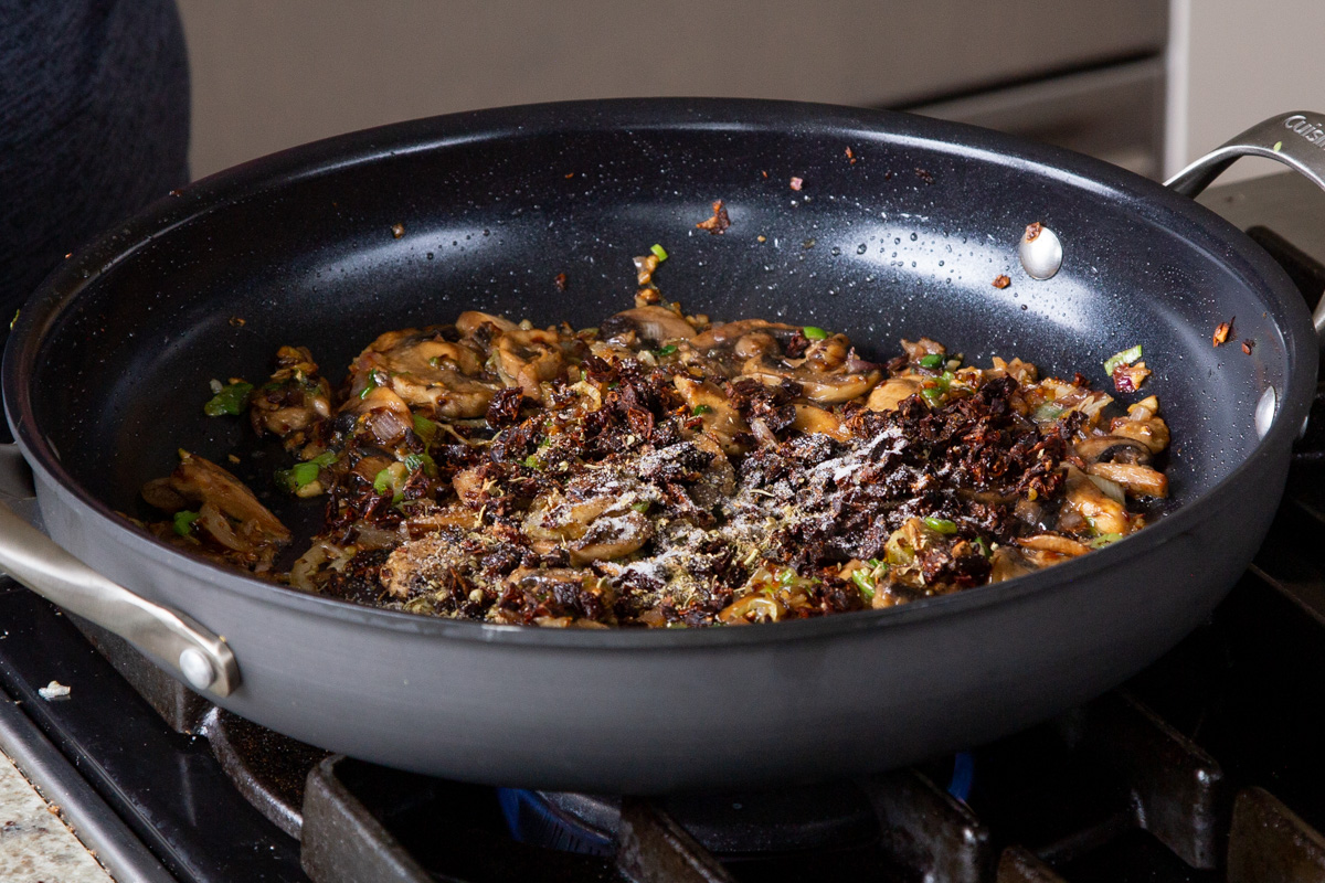 adding sun-dried tomato and spices to the pan of cooked mushrooms