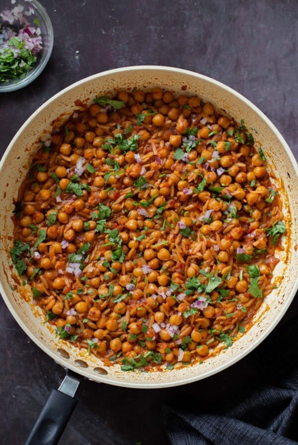 cajun orzo chickpeas in the pan after cooking with fresh herbs and onion on top