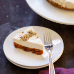 slice of carrot cake cheesecake on a plate next to the full cake