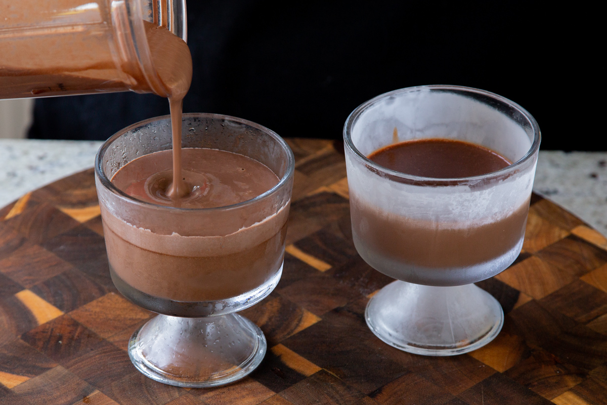 pouring mousse over the dark chocolate mixture in cups