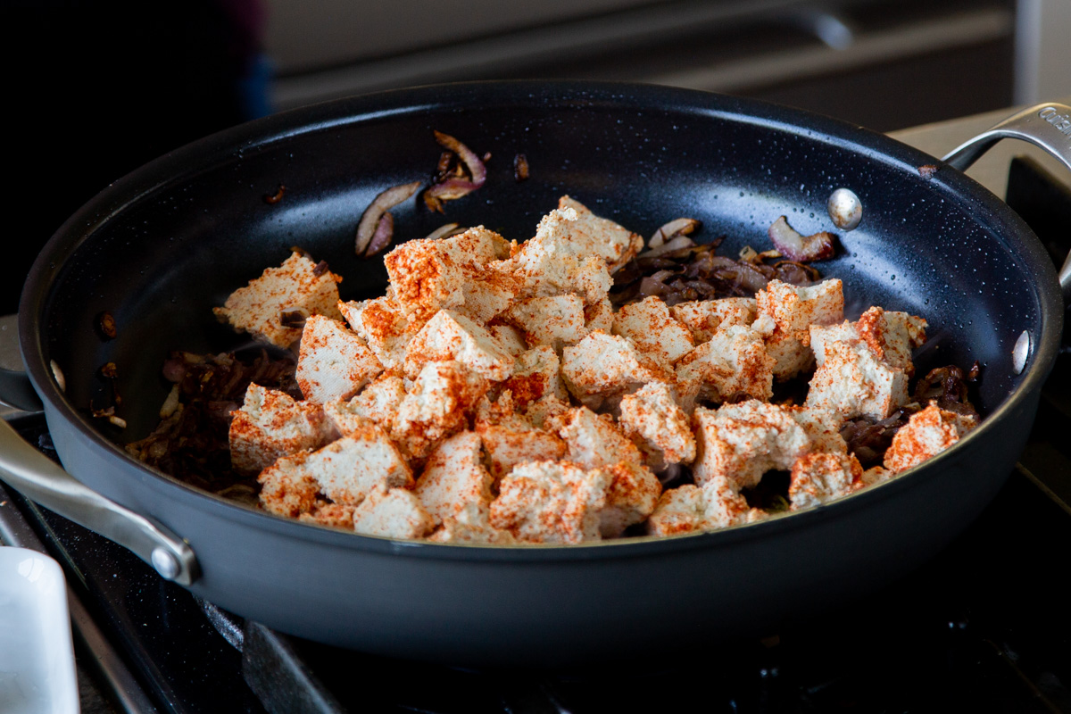 adding the spiced tofu to the pan with the onions