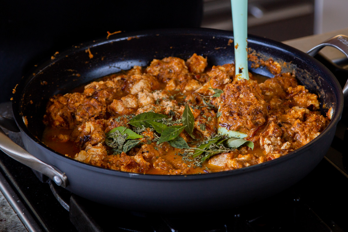 adding curry leaves and fenugreek to the Hyderabadi chicken curry in the pan