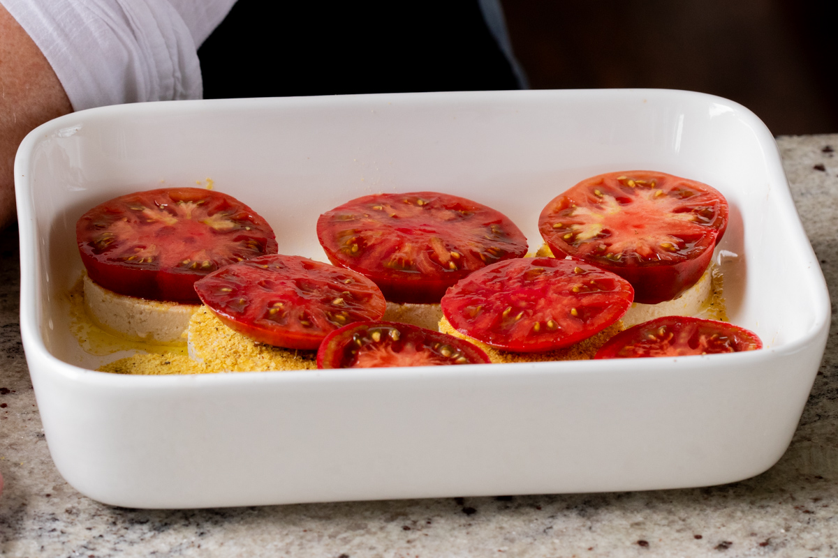 adding tomato slices to the stacks in the baking pan