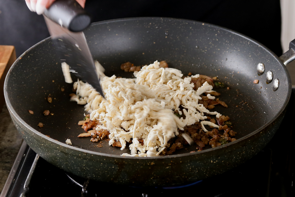 adding shredded tofu to the pan with onion