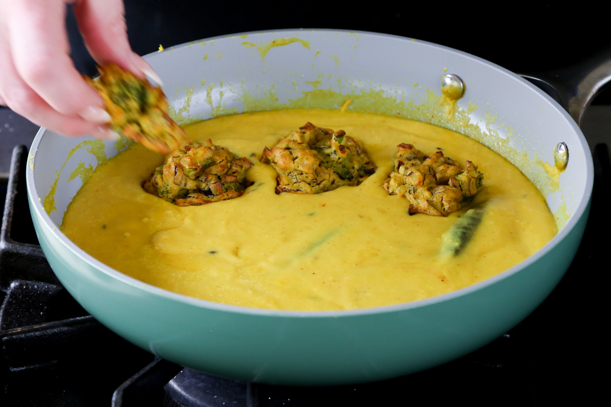 adding pakora to the pan of curry sauce