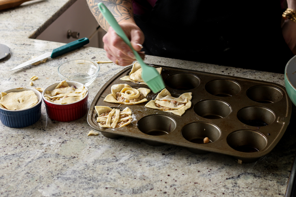 adding crust to the tops of the mini pot pies and brushing on oil before baking