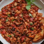 close-up of puttanesca beans on a plate with garlic bread