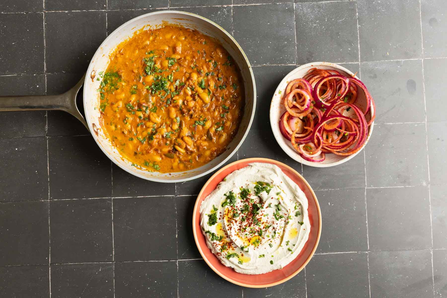chili garlic beans, onion salad, and whipped tofu in bowls on a black table